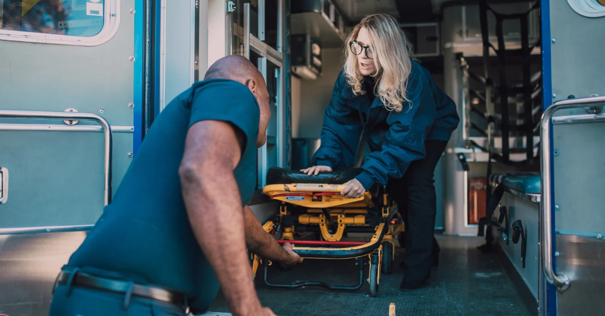 A man helping a woman place a stretcher into an ambulance.